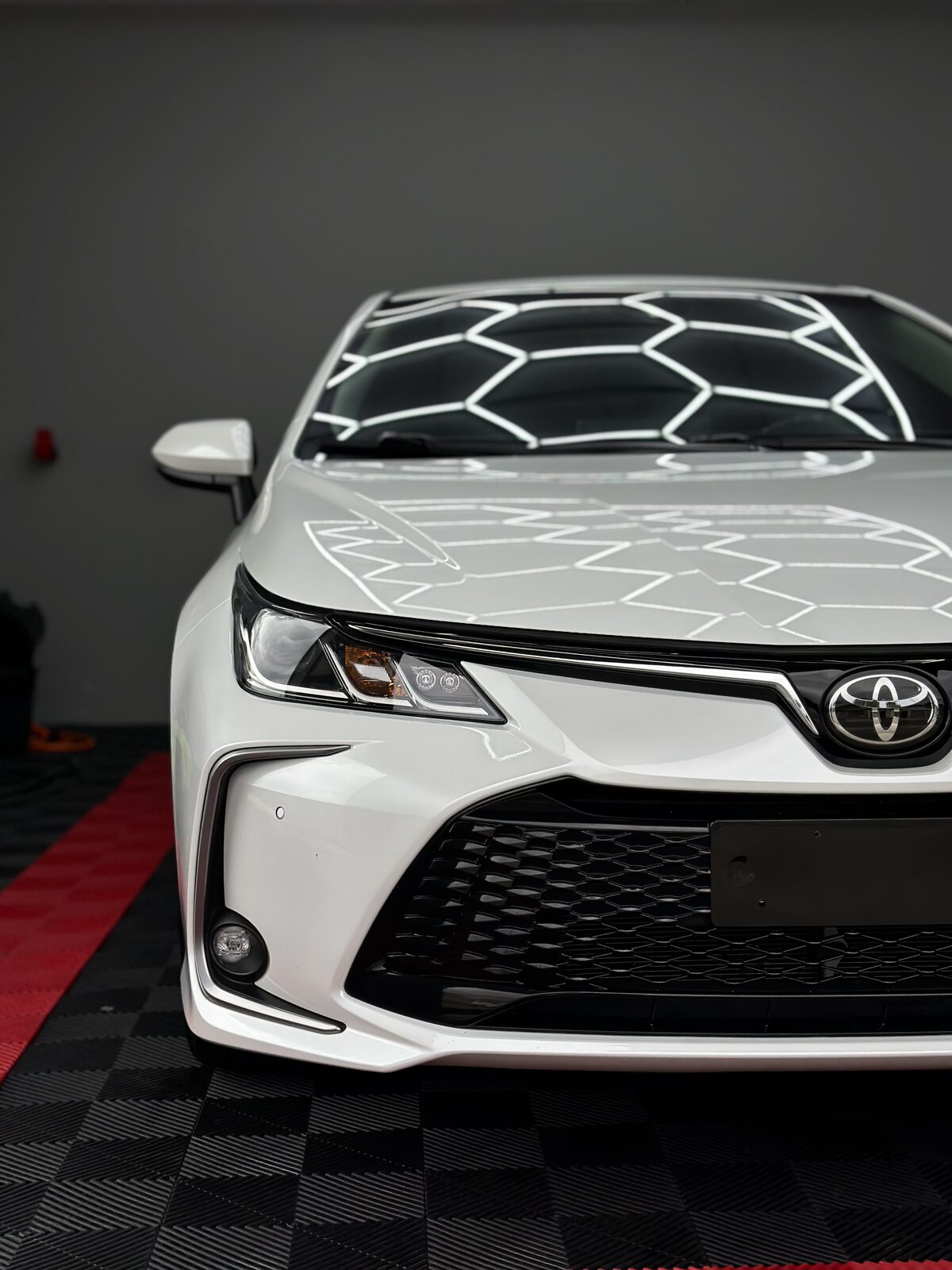 Toyota Corolla branco com pintura vitrificada refletindo a iluminação do estúdio da Bolela em Pinhais - PR